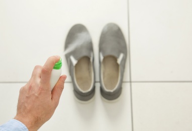 Photo of Man spraying deodorant over pair of shoes at home, closeup. Space for text