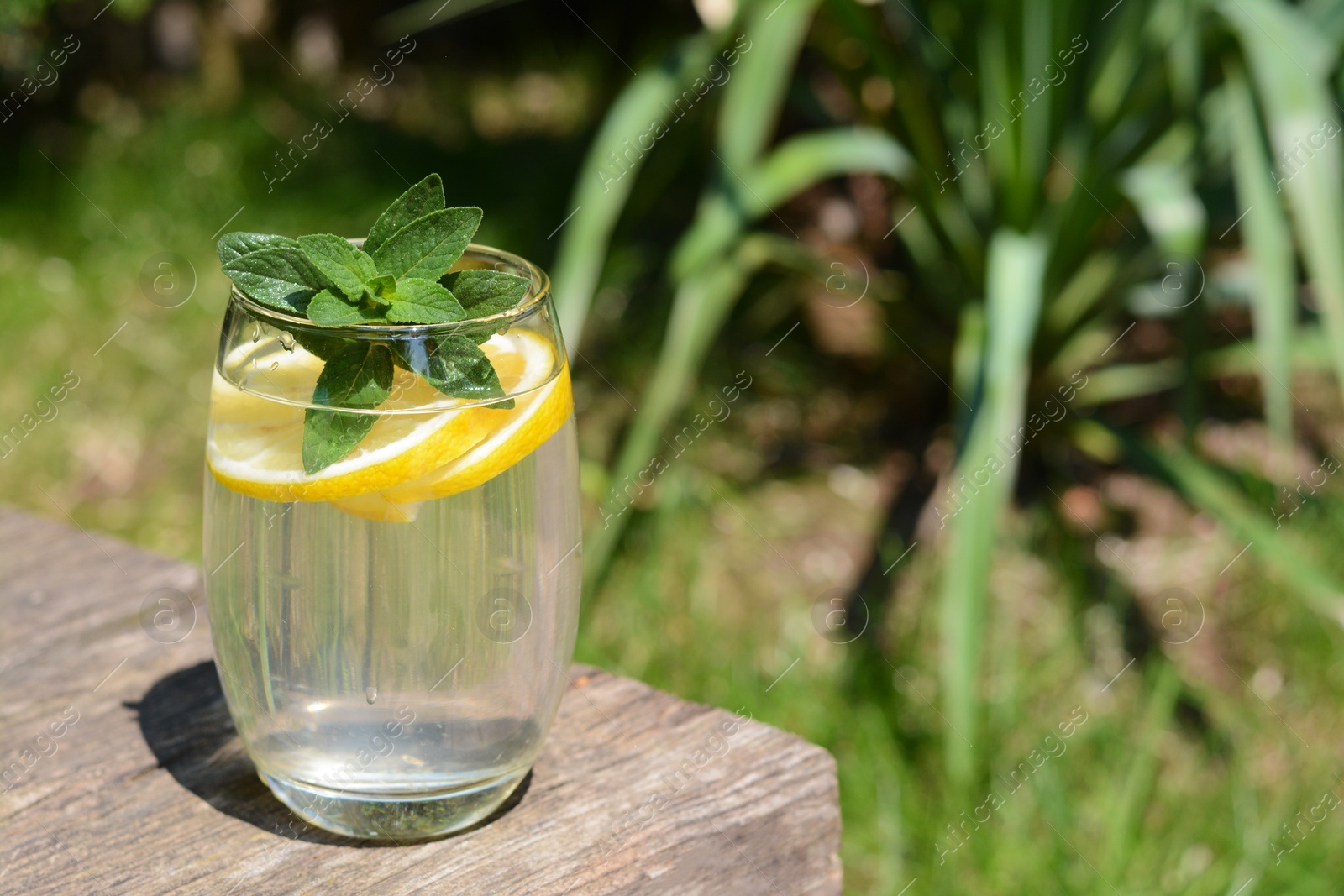 Photo of Refreshing water with lemon and mint on wooden table outdoors, space for text