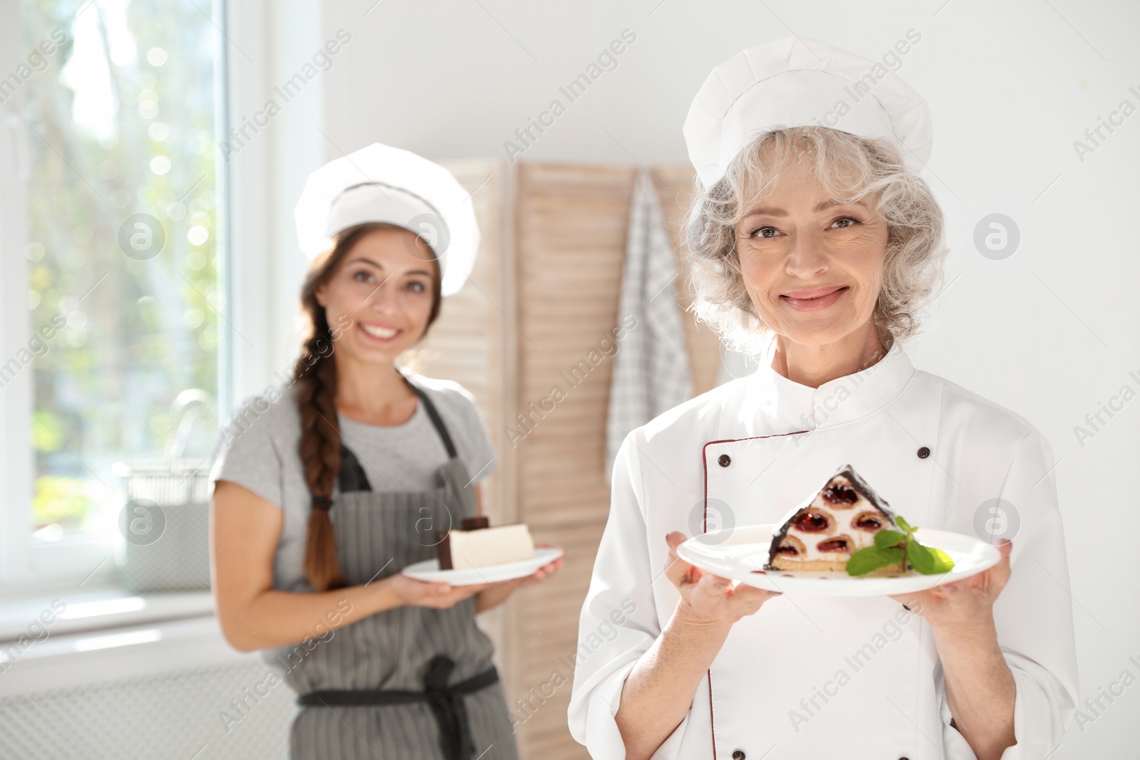 Photo of Professional female chef and trainee with delicious desserts in kitchen