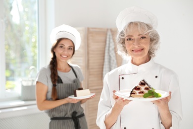 Professional female chef and trainee with delicious desserts in kitchen