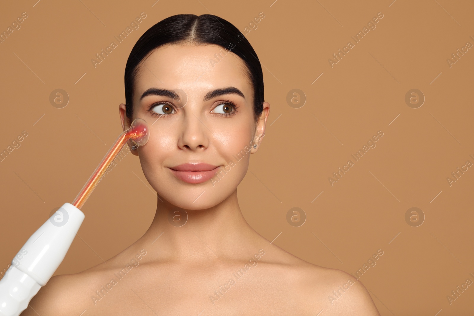 Photo of Woman using high frequency darsonval device on beige background. Space for text