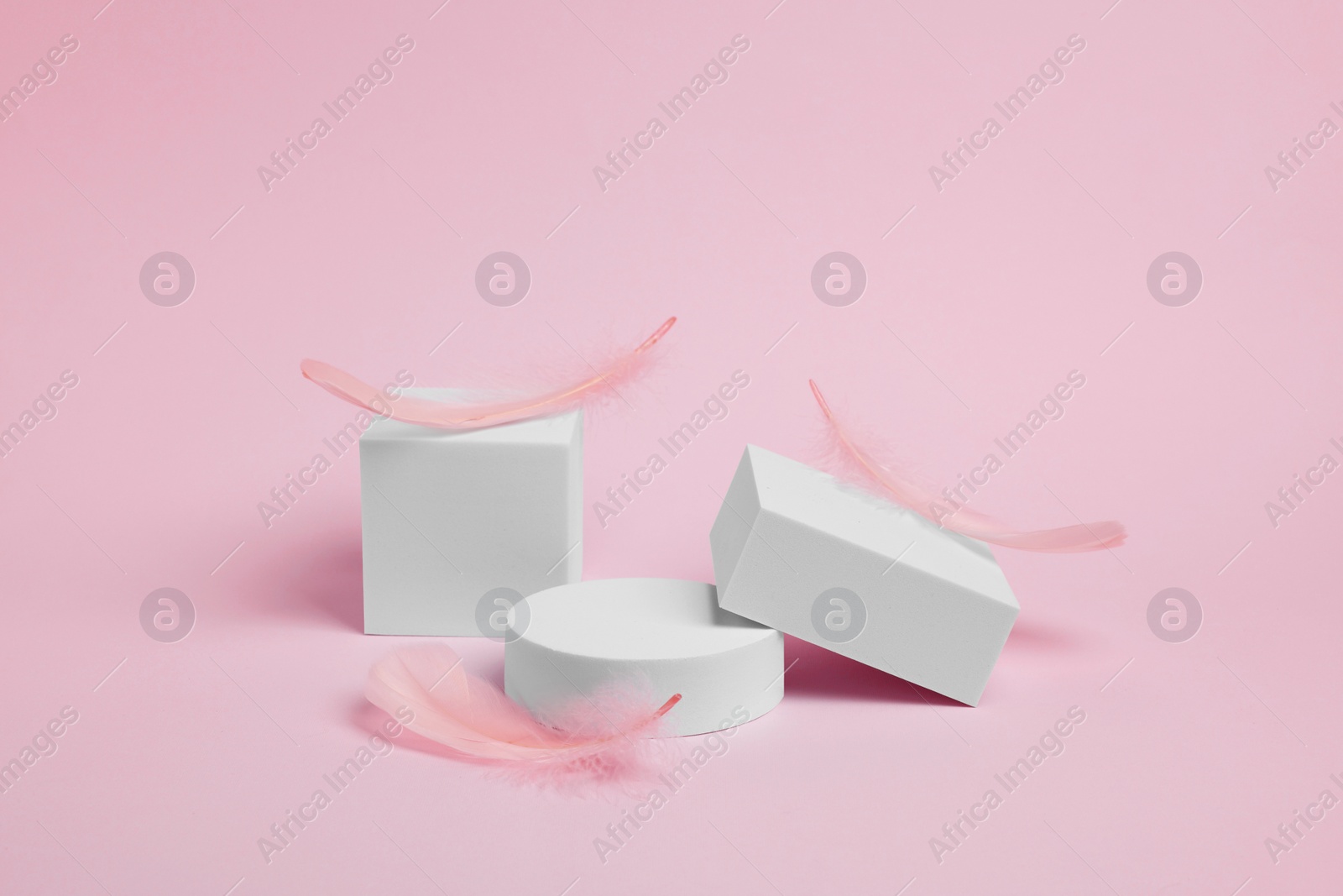Photo of Scene for product presentation. Podiums of different geometric shapes and decorative feathers on pink background