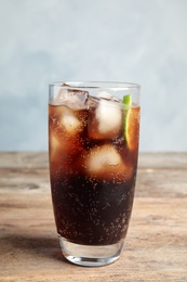 Photo of Glass of refreshing soda drink with ice cubes and lime on wooden table against blue background