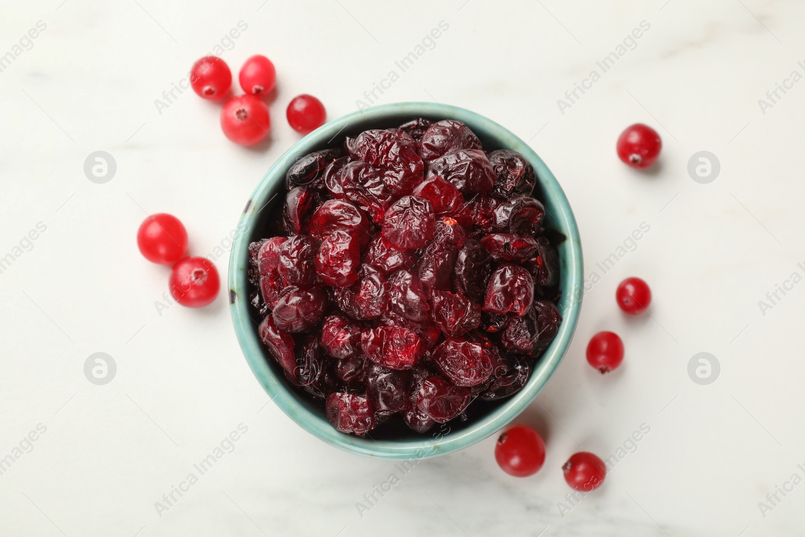 Photo of Tasty dried cranberries in bowl and fresh ones on white table, top view