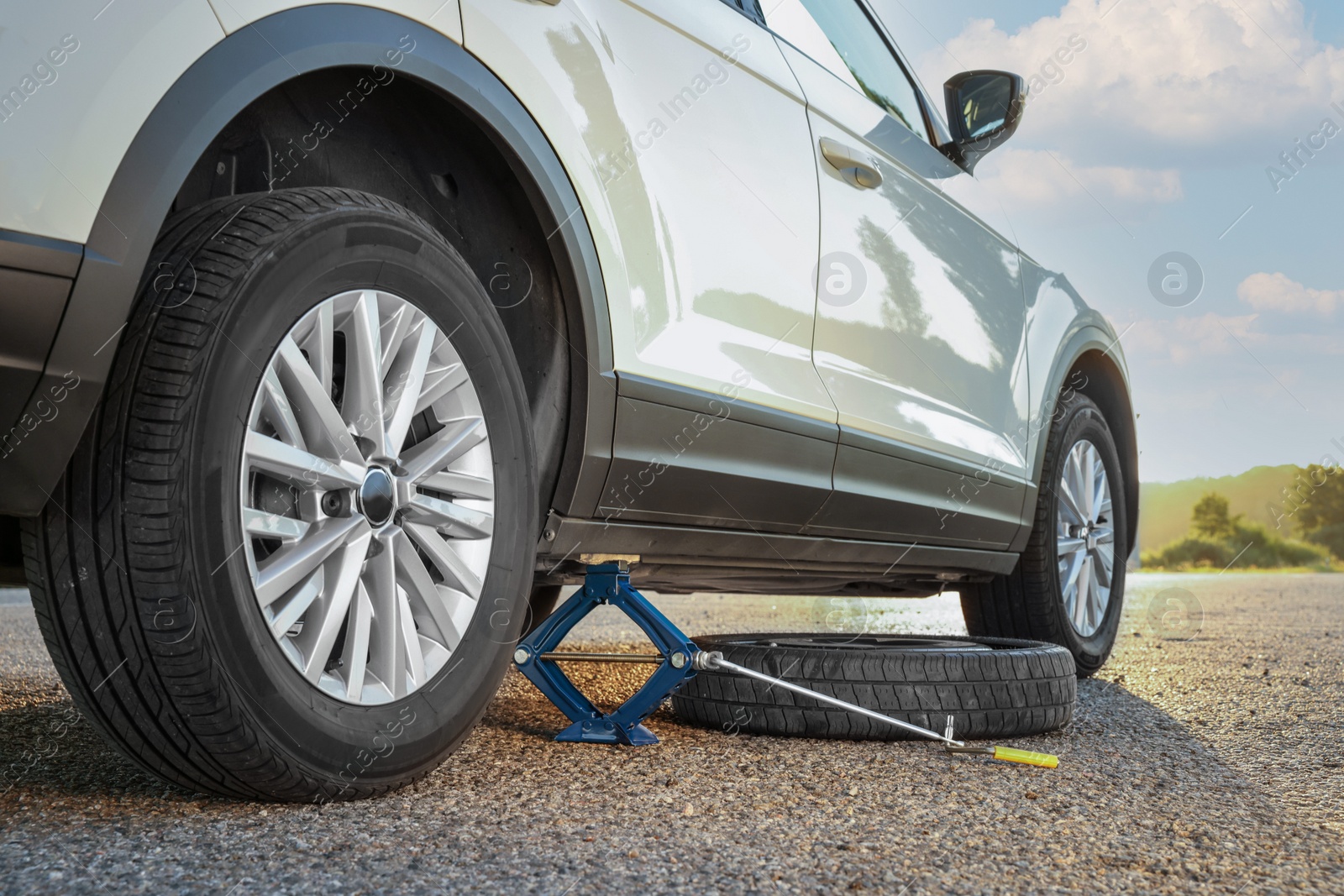 Photo of Car lifted by scissor jack and spare wheel on roadside