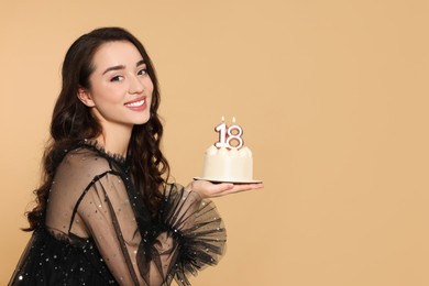 Photo of Coming of age party - 18th birthday. Smiling woman holding delicious cake with number shaped candles on beige background, space for text