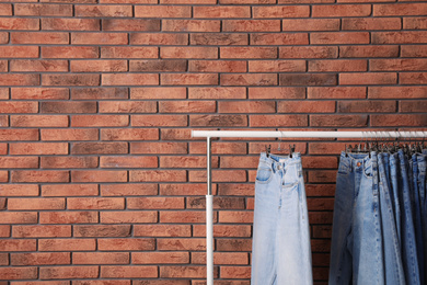 Rack with stylish jeans near brick wall. Space for text