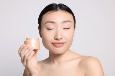 Photo of Beautiful young Asian woman holding jarbody cream on light grey background