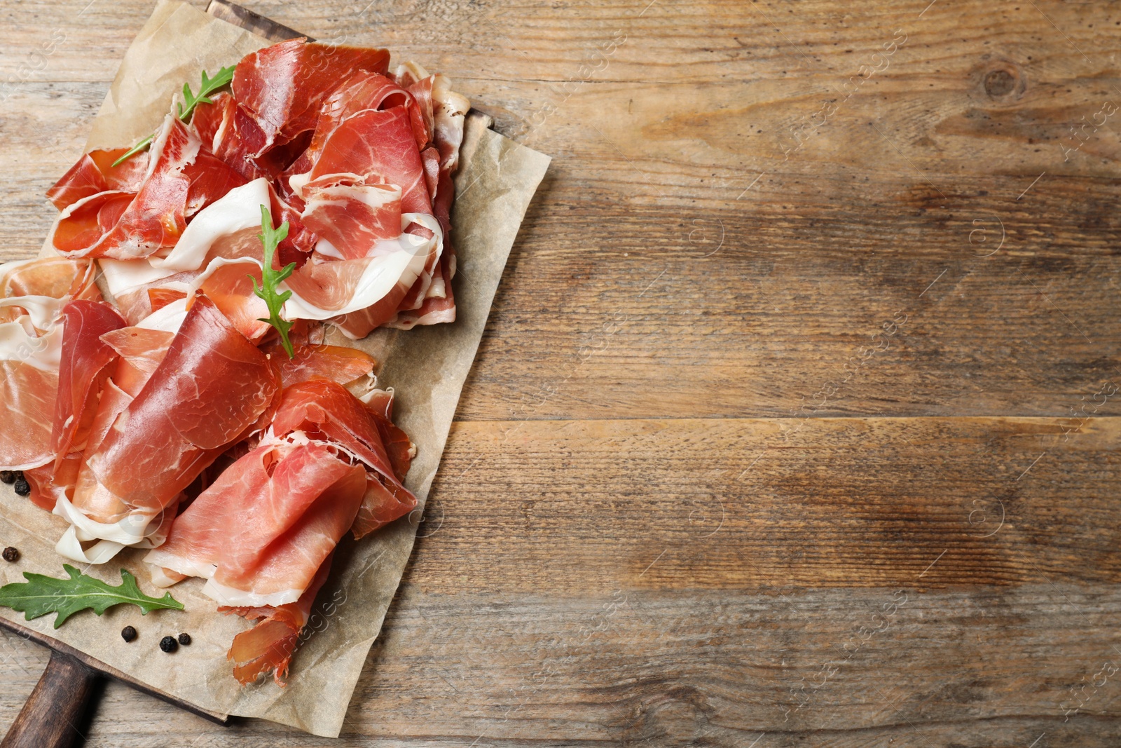 Photo of Pile of tasty prosciutto on wooden table, top view. Space for text