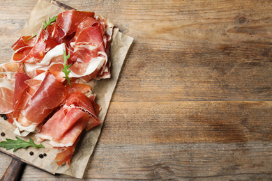 Pile of tasty prosciutto on wooden table, top view. Space for text