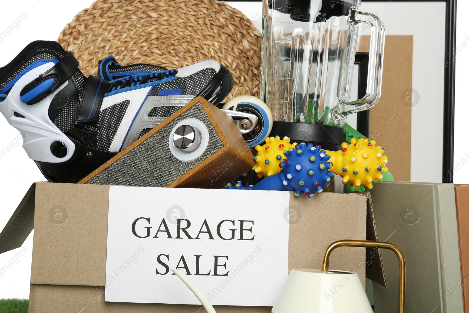 Photo of Box with sign Garage Sale and different stuff against white background, closeup