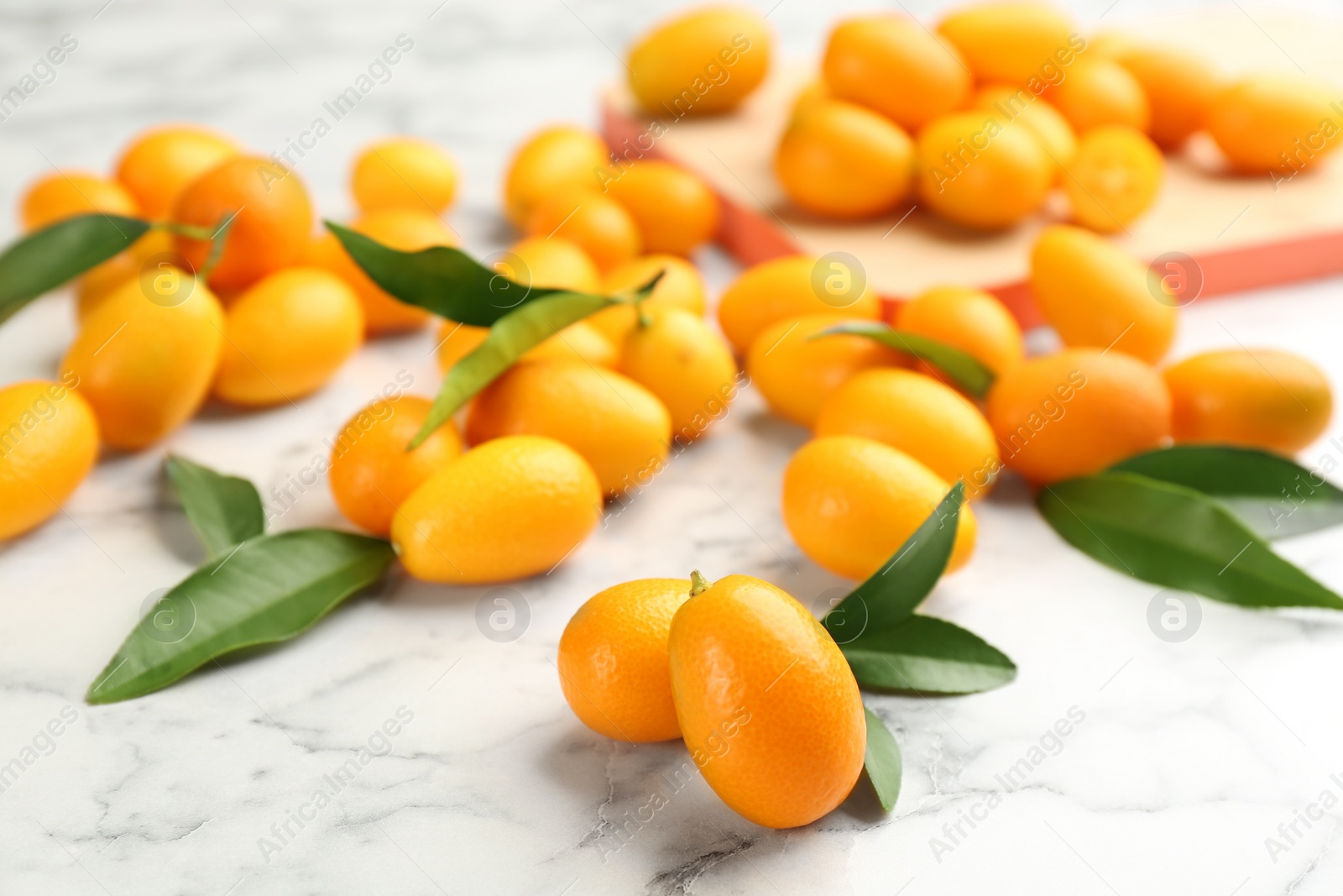 Photo of Fresh ripe kumquats and leaves on white marble table, closeup