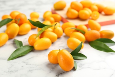 Fresh ripe kumquats and leaves on white marble table, closeup
