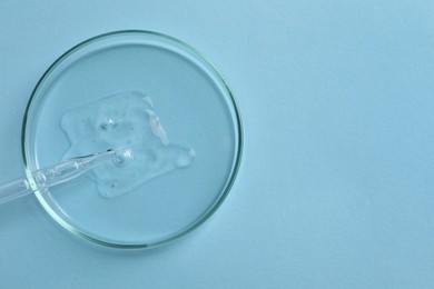 Petri dish with sample of cosmetic oil and pipette on light blue background, top view. Space for text