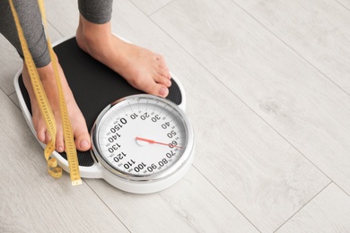 Photo of Woman with tape standing on scales indoors, space for text. Overweight problem