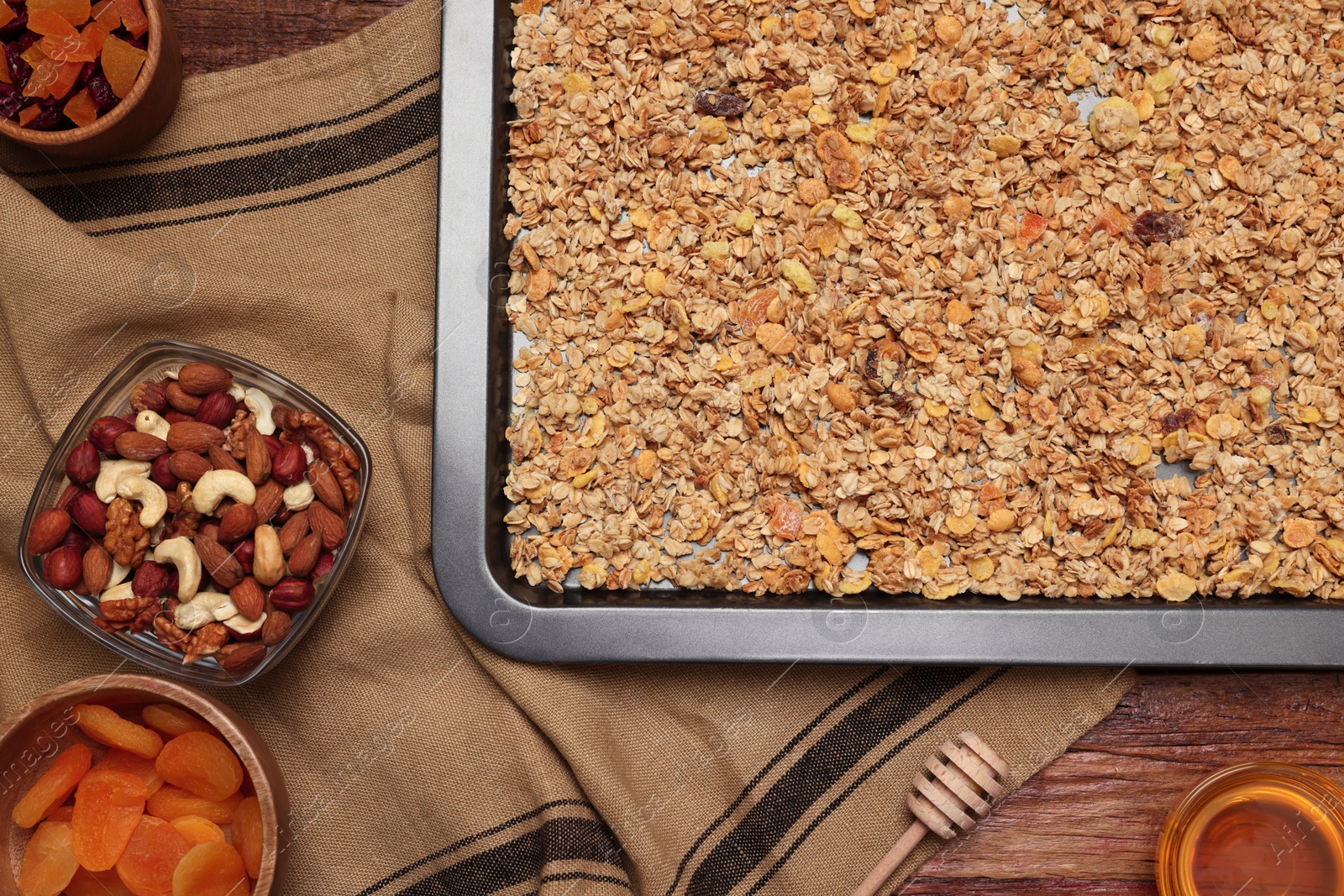 Photo of Making granola. Baking tray with mixture of oat flakes and other ingredients on wooden table, flat lay