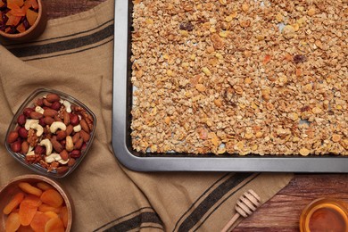 Photo of Making granola. Baking tray with mixture of oat flakes and other ingredients on wooden table, flat lay