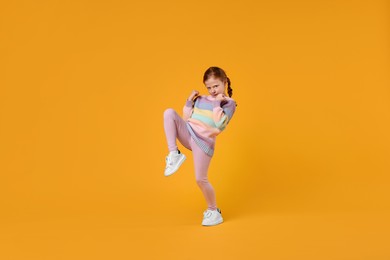 Photo of Cute little girl dancing on orange background