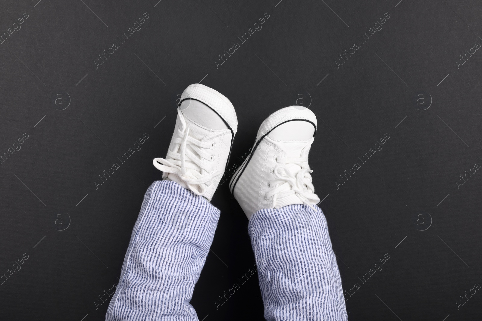 Photo of Little baby in stylish gumshoes on black background, top view