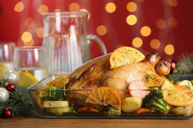 Delicious chicken with oranges and vegetables on table against blurred festive lights, closeup