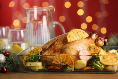 Photo of Delicious chicken with oranges and vegetables on table against blurred festive lights, closeup