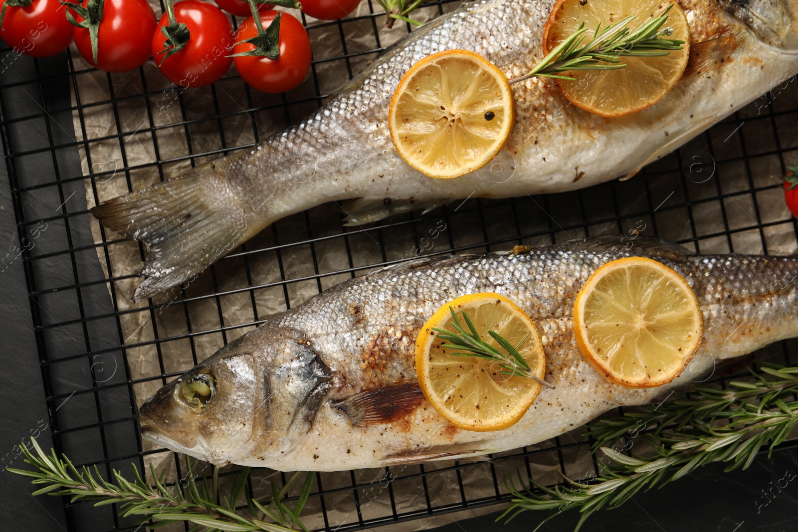 Photo of Baked fish with tomatoes, rosemary and lemon on black textured table, flat lay