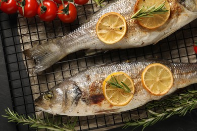 Baked fish with tomatoes, rosemary and lemon on black textured table, flat lay