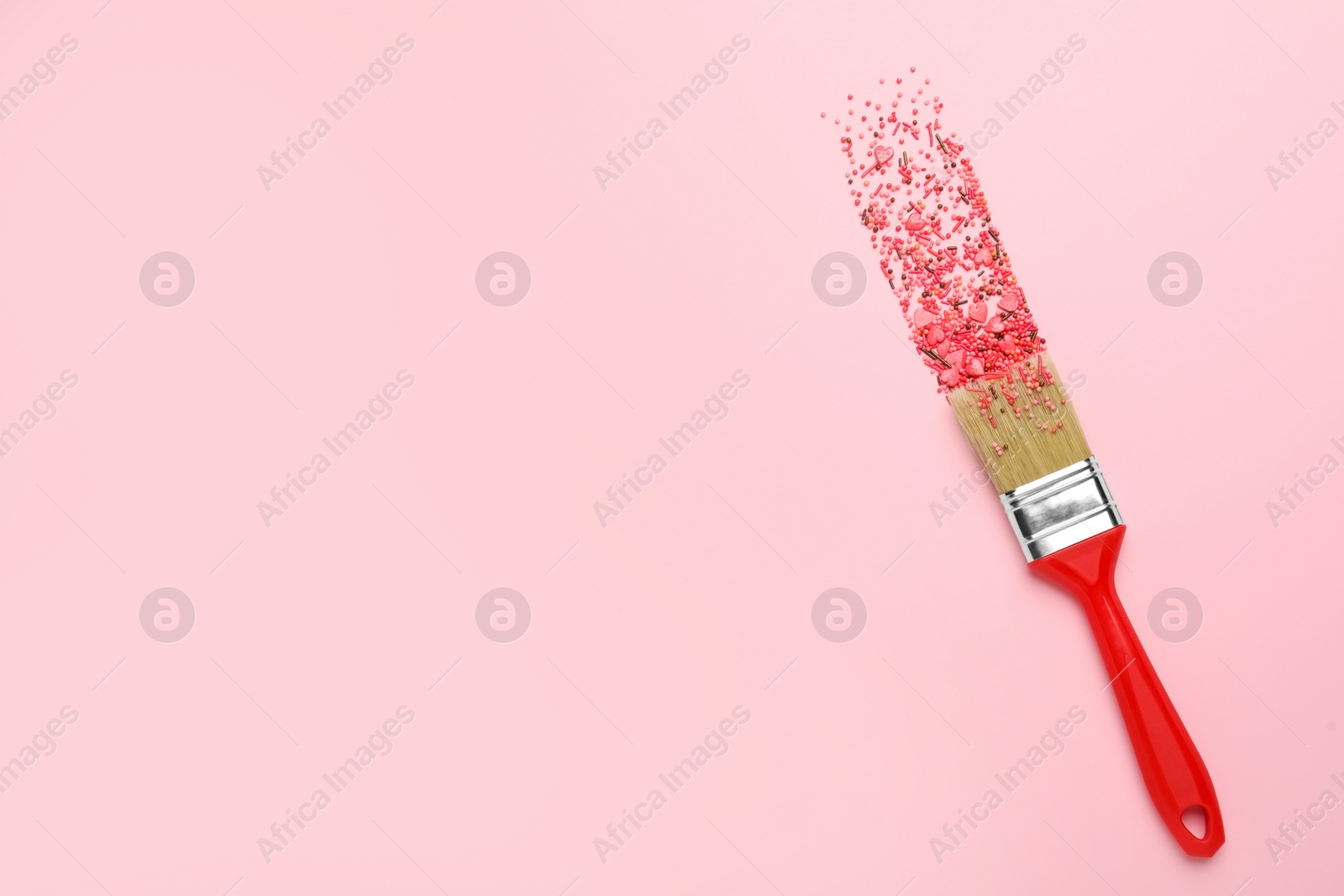 Photo of Brush painting with red sprinkles on pink background, top view. Space for text. Creative concept