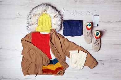 Set of warm clothes and mobile phone on wooden background, flat lay. Winter vacation