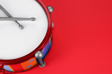 Colorful drum and sticks on red background, above view with space for text. Percussion musical instrument