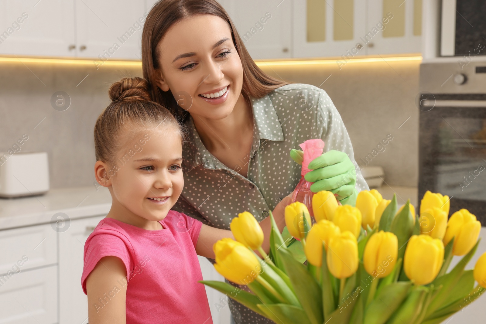 Photo of Spring cleaning. Mother and daughter spraying beautiful bouquet of yellow tulips with water at home