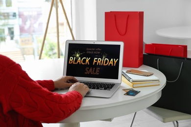 Photo of Woman shopping online using laptop at table indoors, closeup. Black Friday Sale