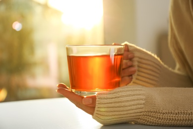 Woman holding glass cup of tea at table at home, closeup