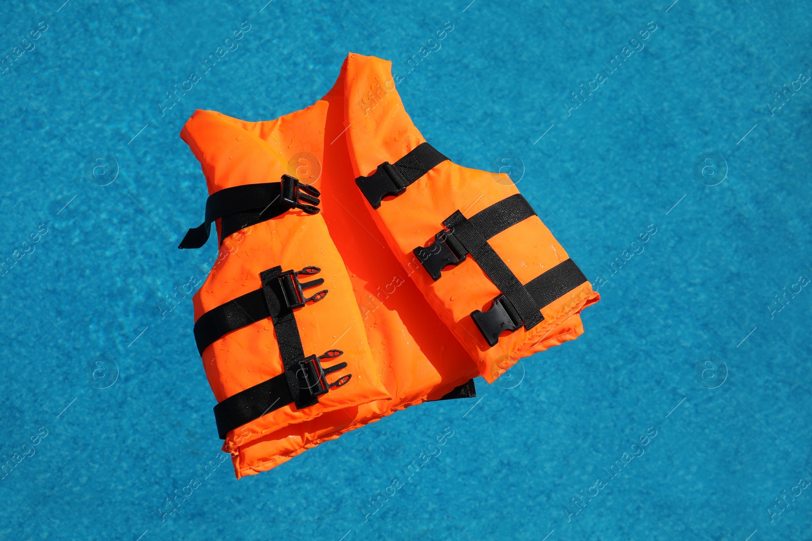 Photo of Bright orange life jacket floating in swimming pool, top view