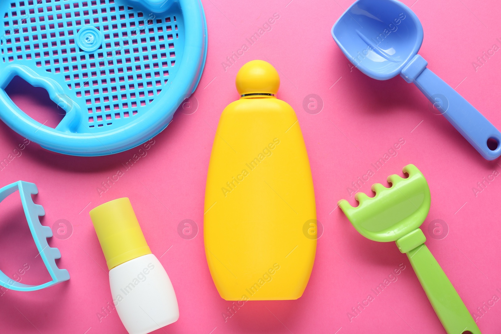 Photo of Bottle of suntan cream and children's beach toys on pink background, flat lay