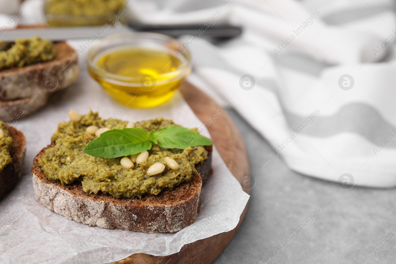 Photo of Tasty bruschettas with pesto sauce, nuts and fresh basil on light grey table, closeup. Space for text