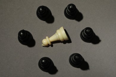 Photo of Black chess pieces and white one on grey background, flat lay. Bullying concept