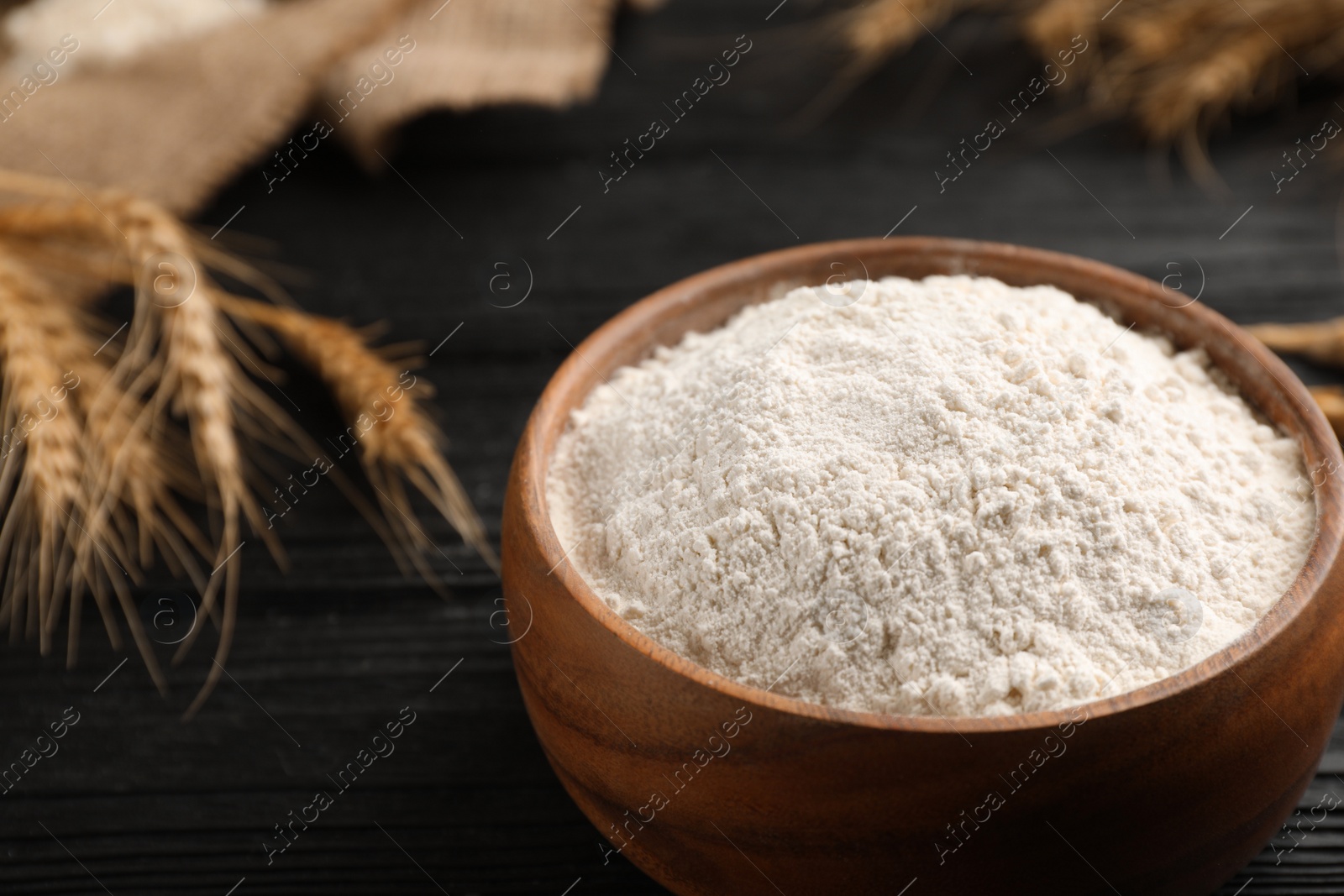 Photo of Bowl of flour on black wooden table, closeup. Space for text