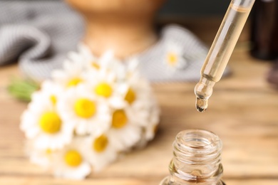 Pipette with essential oil over bottle on blurred background, closeup. Space for text