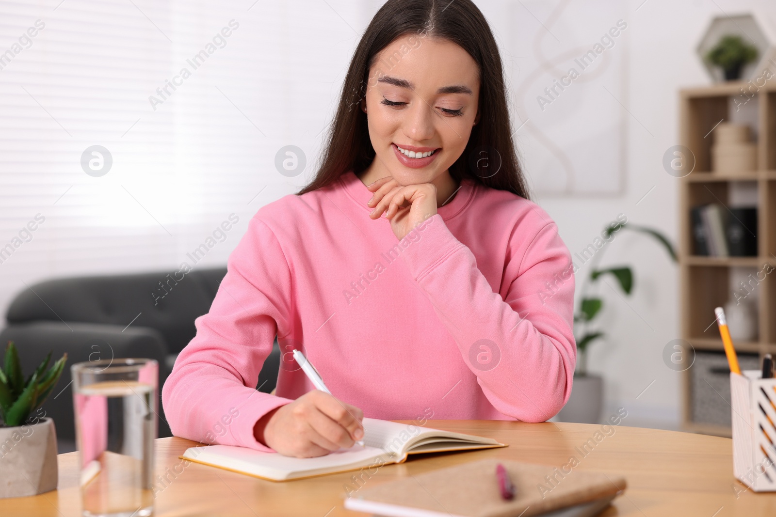 Photo of Young woman writing in notebook at wooden table indoors