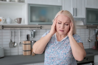 Photo of Mature woman suffering from headache in kitchen