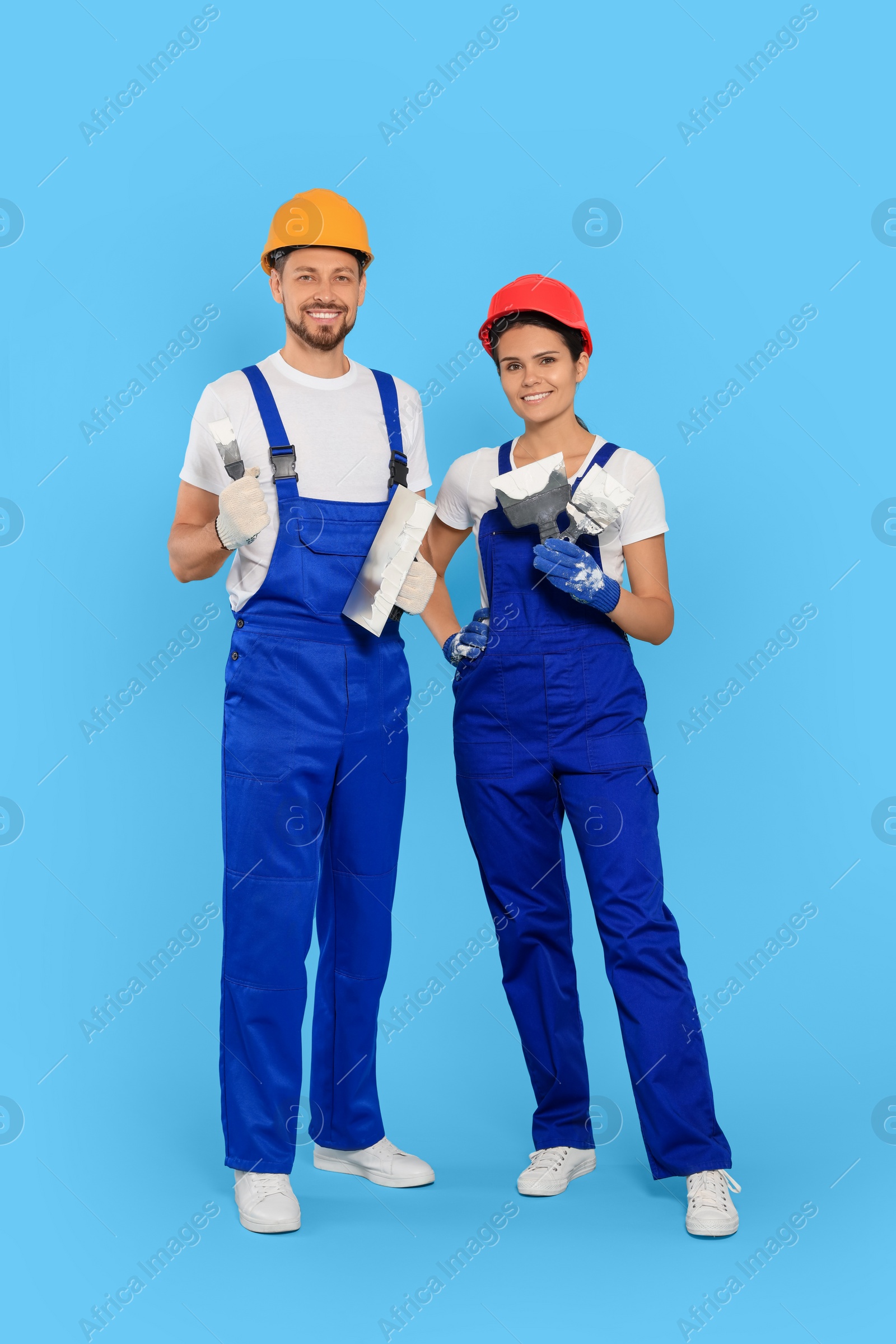 Photo of Professional workers with putty knives in hard hats on light blue background