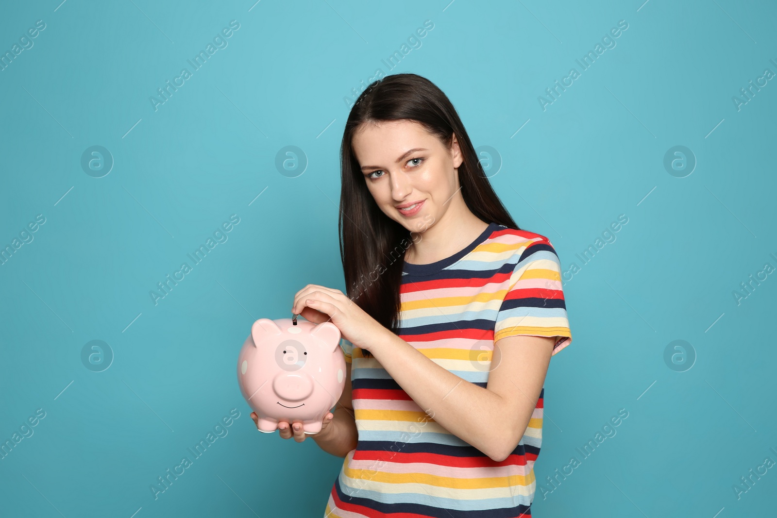 Photo of Young woman putting coin into piggy bank on color background