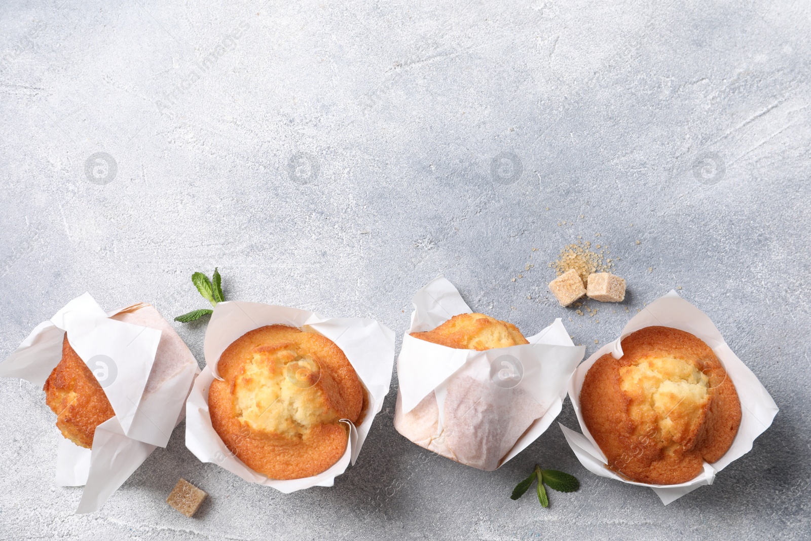 Photo of Delicious sweet muffins and brown sugar on light grey textured table, flat lay. Space for text