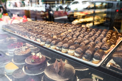 Photo of Different delicious cakes on display in cafe, view through window