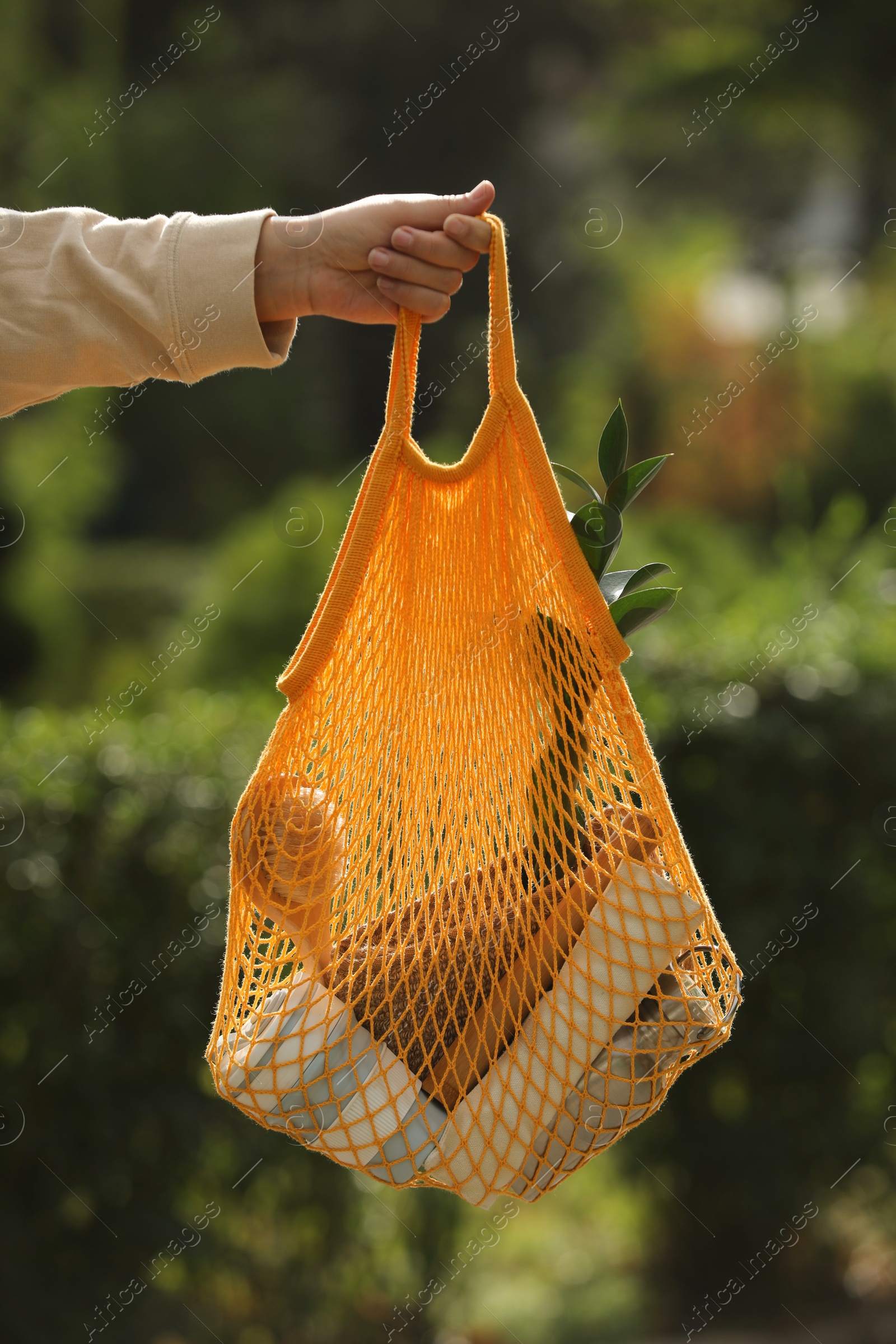 Photo of Conscious consumption. Woman with net bag of eco friendly products outdoors, closeup
