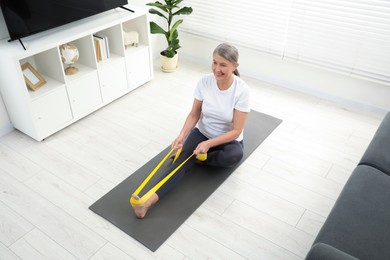 Photo of Senior woman doing exercise with fitness elastic band on mat at home