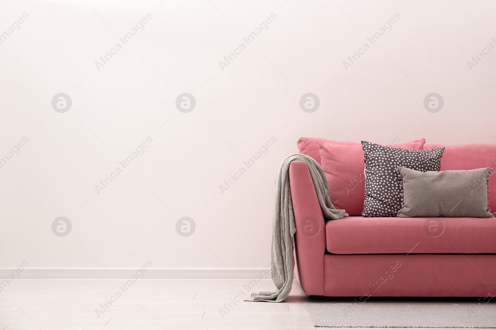 Photo of Comfortable pink sofa near white wall indoors, space for text. Simple interior