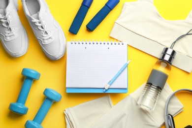 Photo of Flat lay composition with sportswear, notebook and dumbbells on yellow background. Gym workout plan