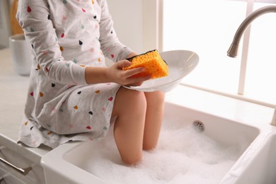 Photo of Naughty girl put her legs into sink while washing dishes in kitchen at home, closeup